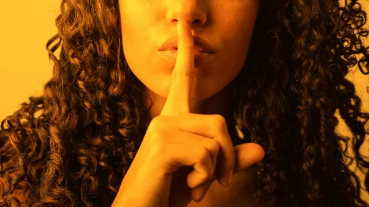 Achtung - streng geheim! - Blog: (Symbolfoto) Zu sehen ist eine Frau, die sich einen Finger an den Mund hält.
